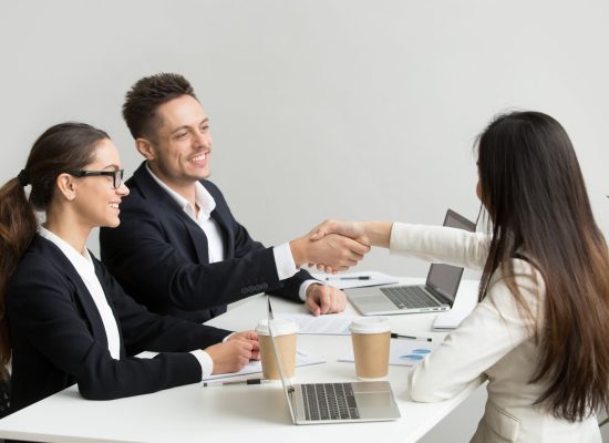 Friendly satisfied partners handshaking at group meeting thanking for successful teamwork, smiling millennial businessman shaking hand greeting businesswoman, respect or making contract deal concept